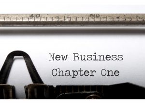 A typewriter typing the following words on paper, "New Business Chapter One"